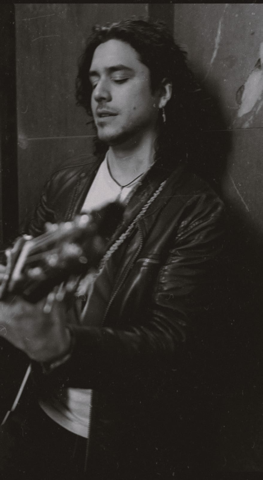 anthony and his guitar against a brick wall in black and white