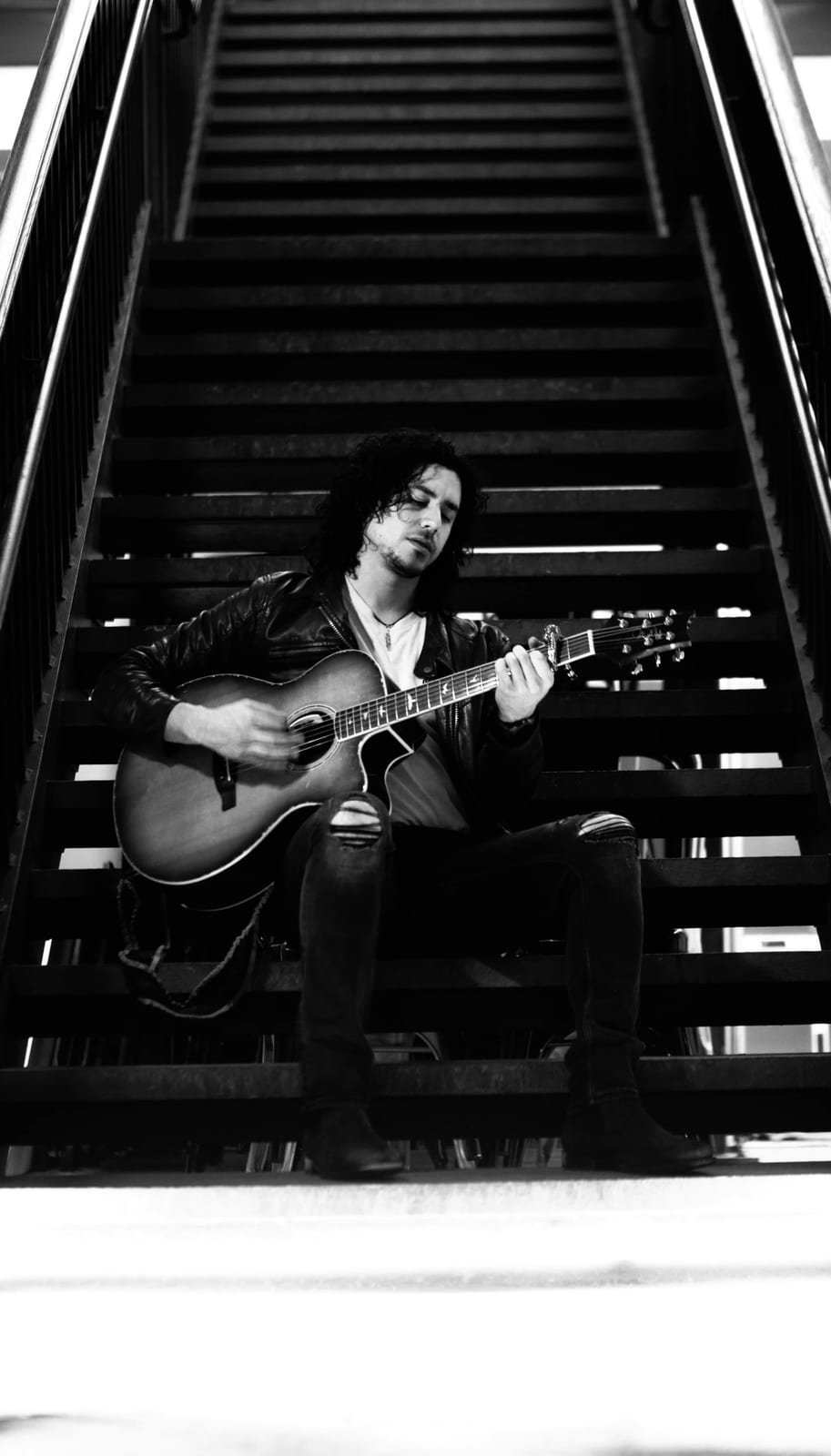 Anthony sitting with his guitar on stairs in black and white